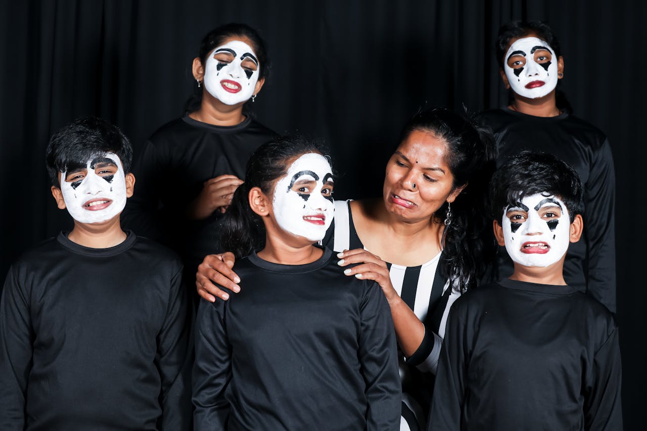 services-01 Children and an adult display expressive mime faces during a theatrical performance indoors.