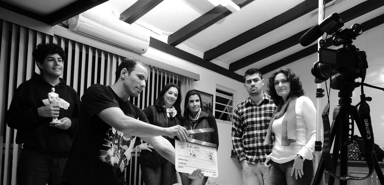 home-hero-2 A group of adults collaborate on a filmmaking project, seen holding a clapperboard indoors.