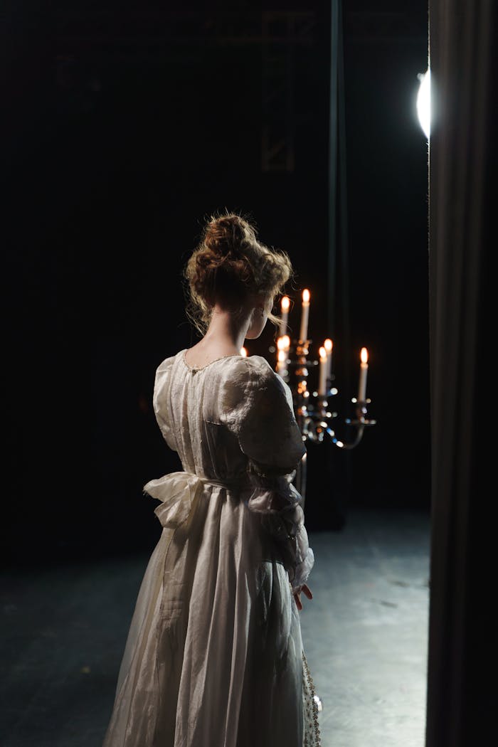 services-01 Rear view of actress in white dress on stage with dramatic candlelight.
