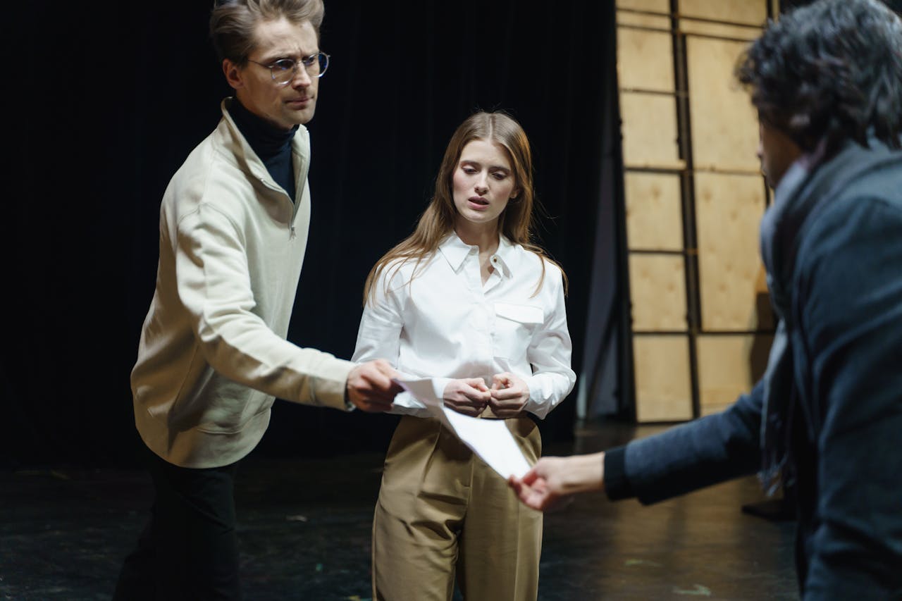 services-03 Actors engage in a rehearsal, exchanging scripts on stage, embodying theatrical drama and emotion.